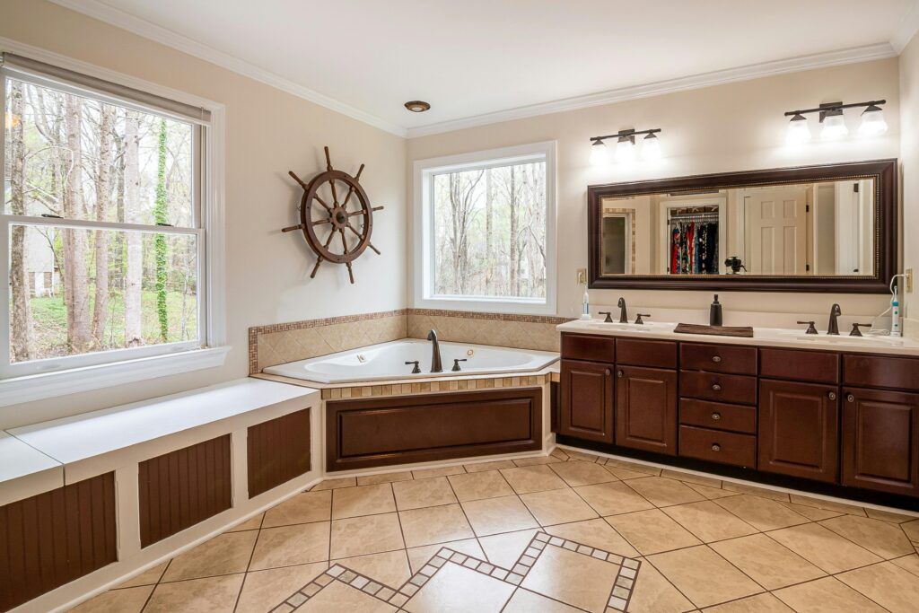 Spacious bathroom featuring a large corner bathtub, wooden cabinets, and natural light from large windows.