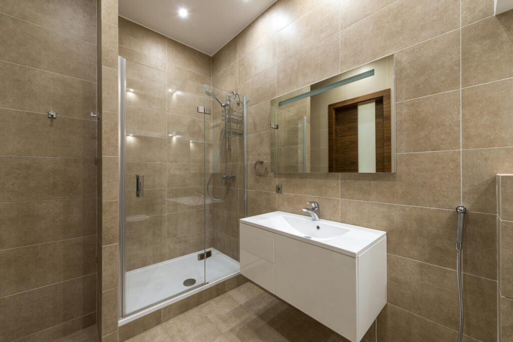 Elegantly designed modern bathroom featuring a glass shower, wall mirror, and large ceramic tiles.