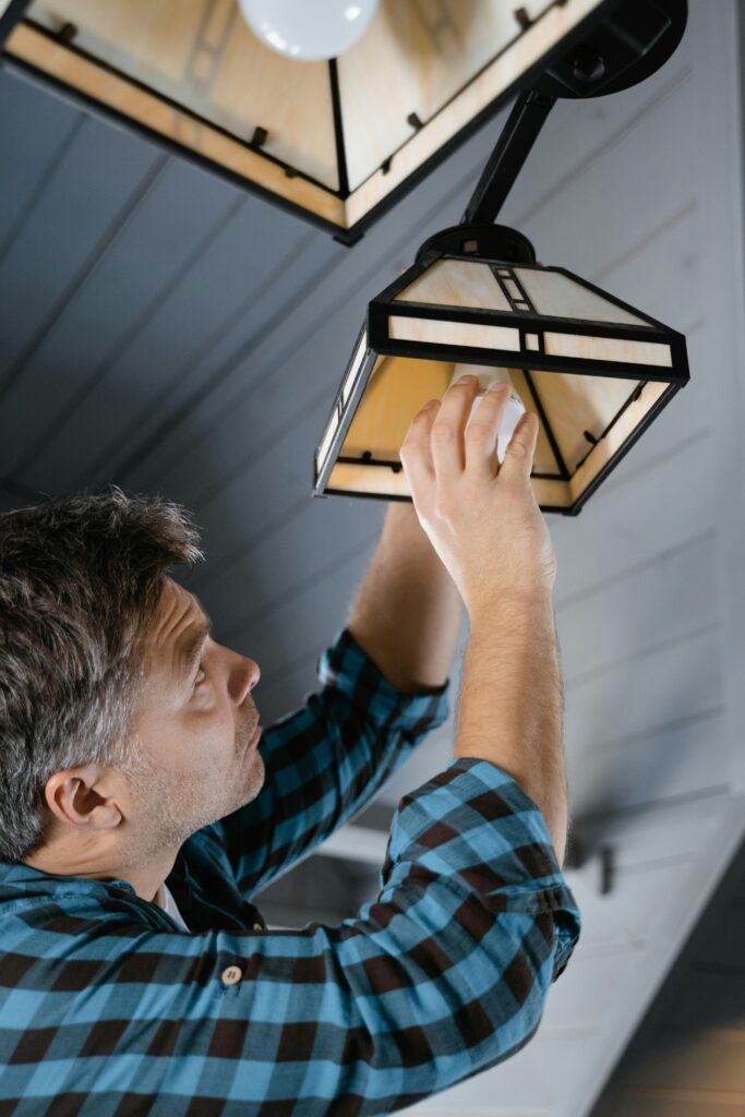 Man in plaid shirt fixing a pendant light indoors.